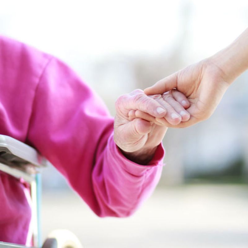 A caregiver is helping an elderly person out of wheel chair.