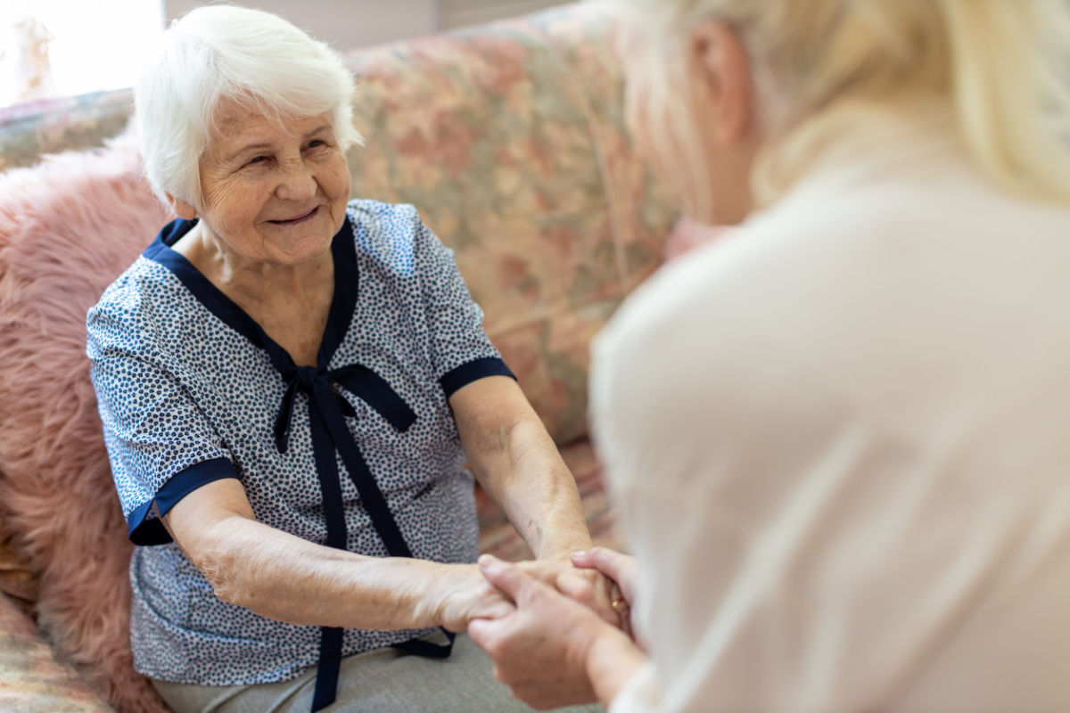 Caregiver gently holds the hands of an elderly woman.