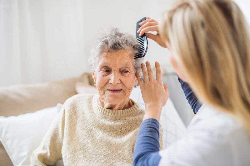 caregiver with senior at home brushing her hair.